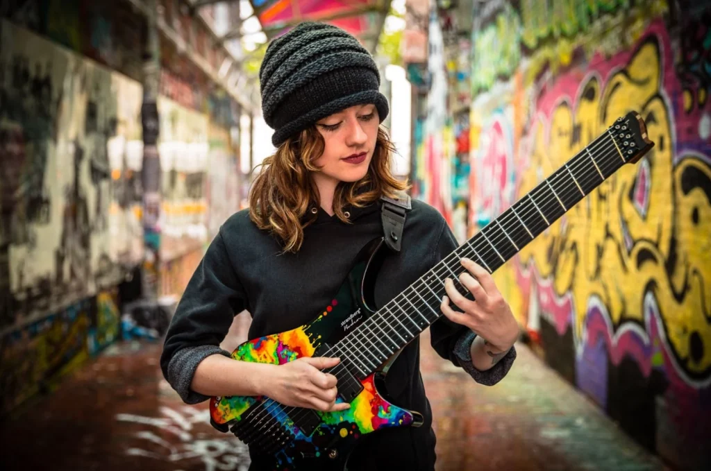 Sarah Longfield playing an eight-string guitar in an alley covered in graffiti 
