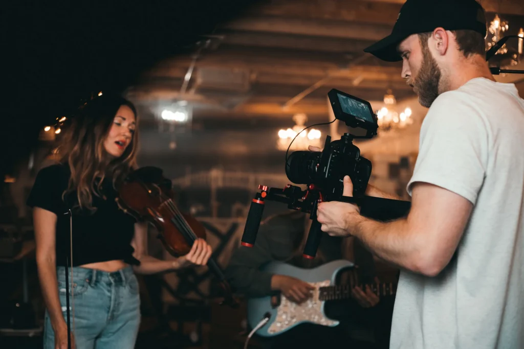 A man filming and recording a woman playing the violin
