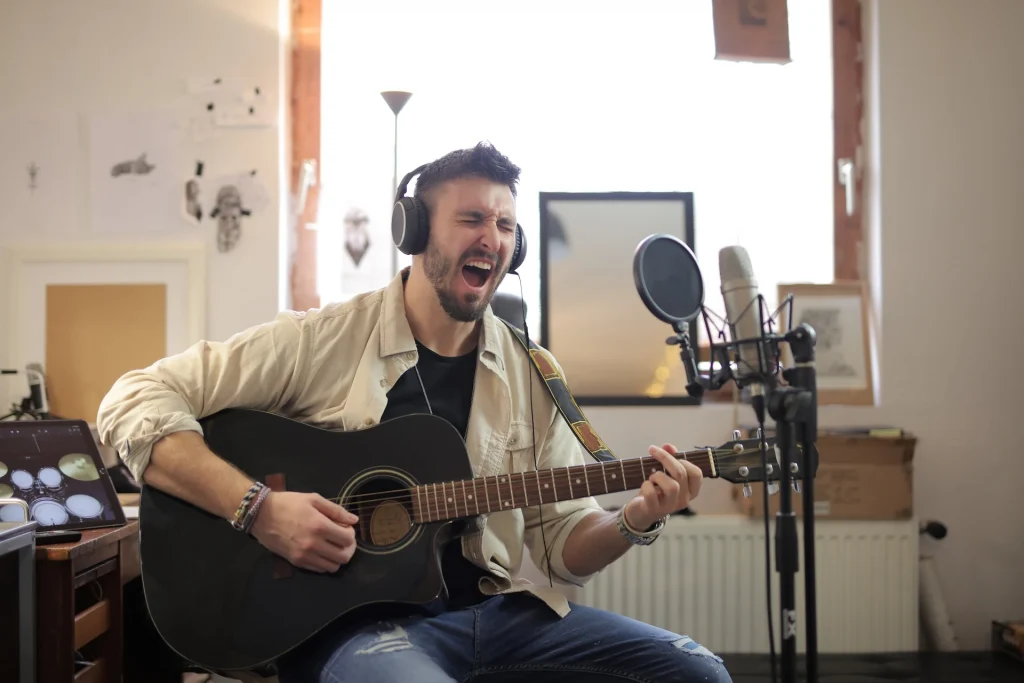 Man sitting playing a guitar and singing into a microphone in his room