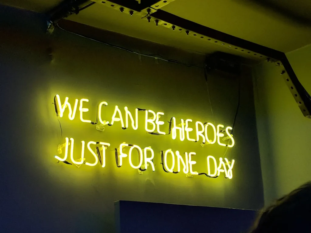 A neon sign that reads "We can be heroes just for one day."
