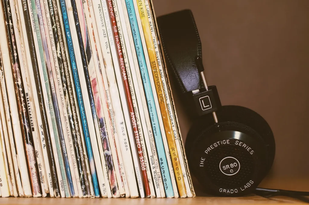 A stack of vinyl records sitting on a shelf with a pair of headphones leaning against them
