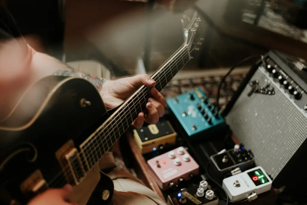 Someone playing the guitar with a bunch of pedals in the background