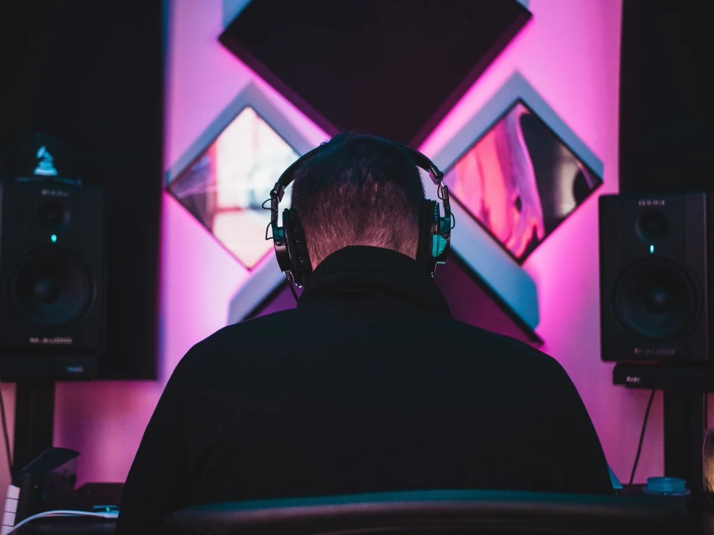 A man wearing headphones sitting in a recording studio with his back facing us