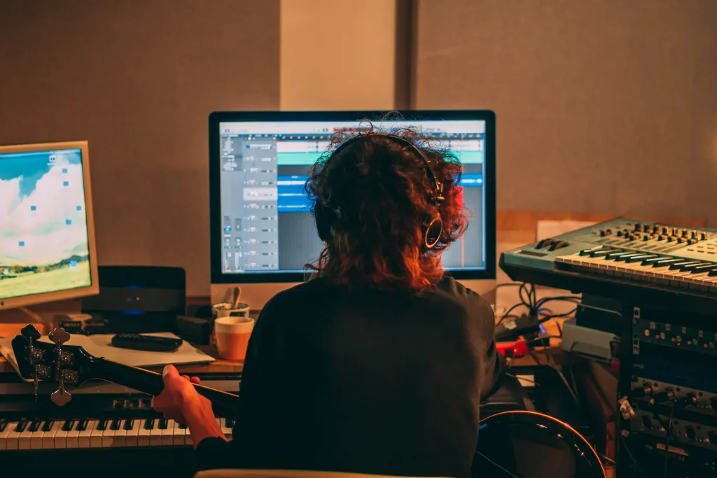 A person sitting in front of a computer with a guitar on their lap