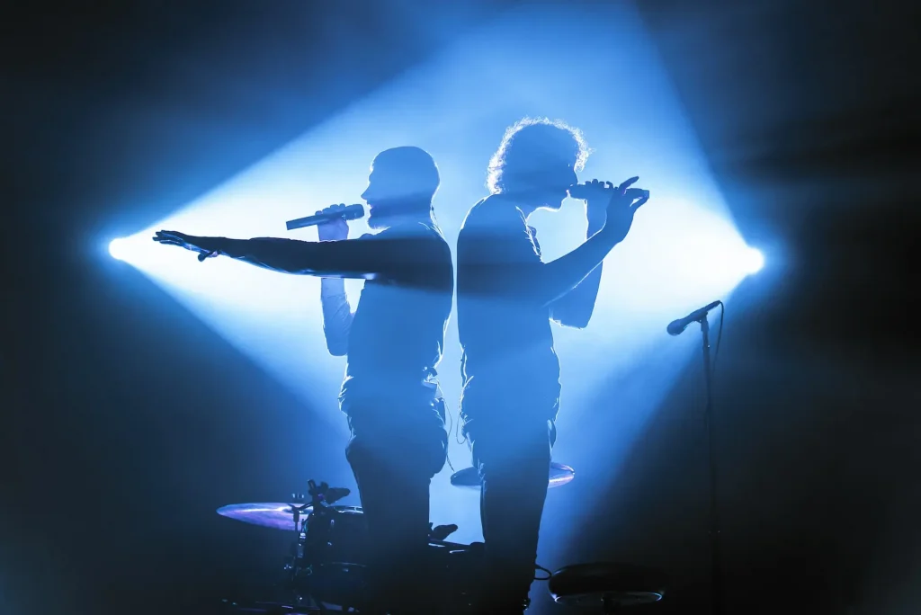 Two men on stage singing into microphones standing back to back