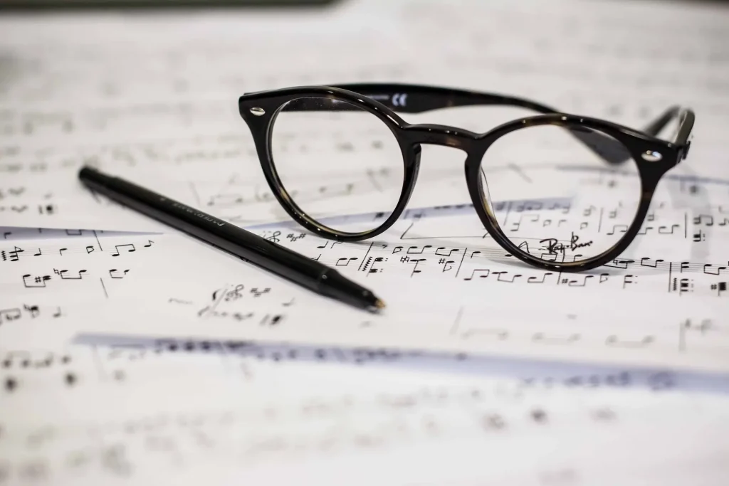 A pair of glasses and a pen on top of a pile of sheet music