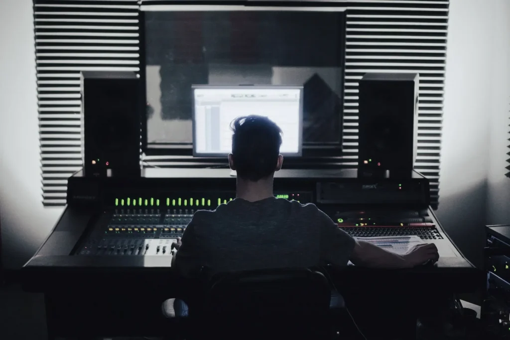 A man sitting in front of a mixing table looking at a computer monitor