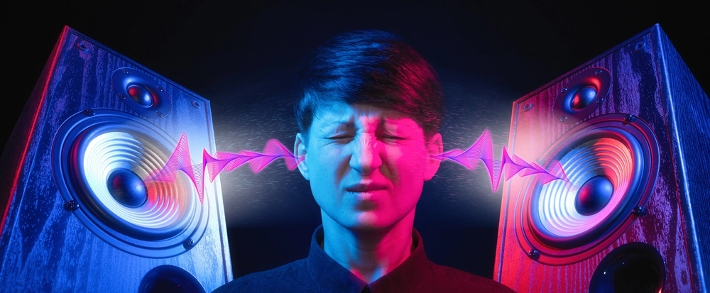 A man at the center with his eyes closed, with sound waves going into his ears from two speakers, one on each side of him