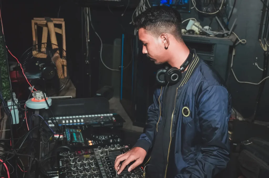 A man wearing headphones around his neck turning a knob on a mixer.