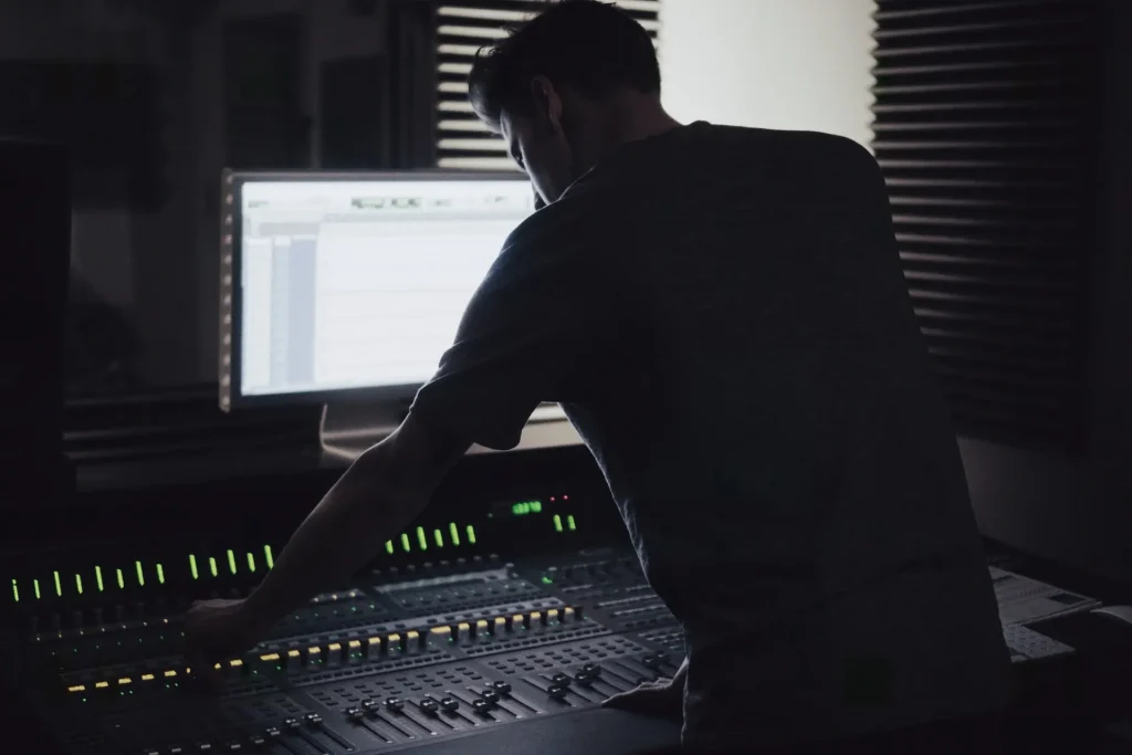 A man leaning over an audio workstation mixer.