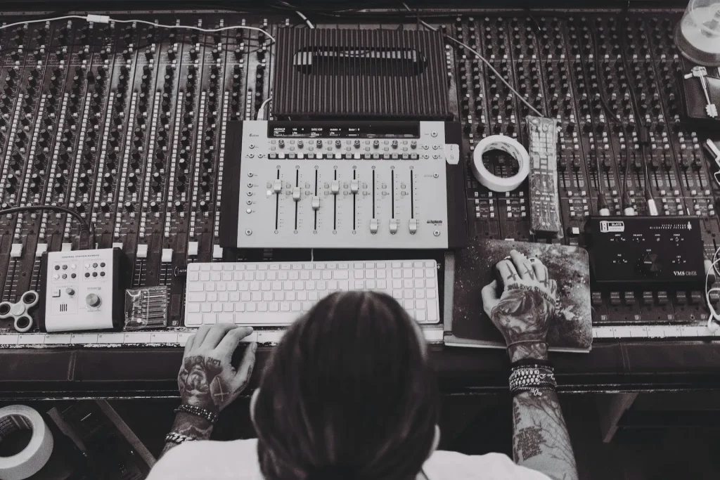 A person working on a computer sitting in front of a mixing console