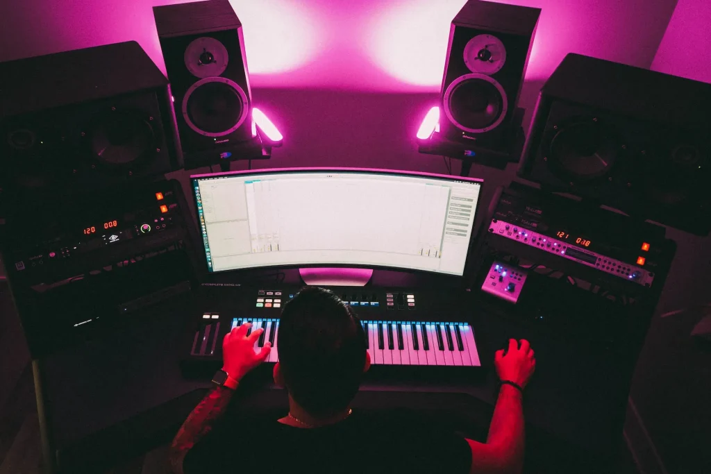 Bird's eye view of a man working at a computer with a piano keyboard on the desk in front of him.