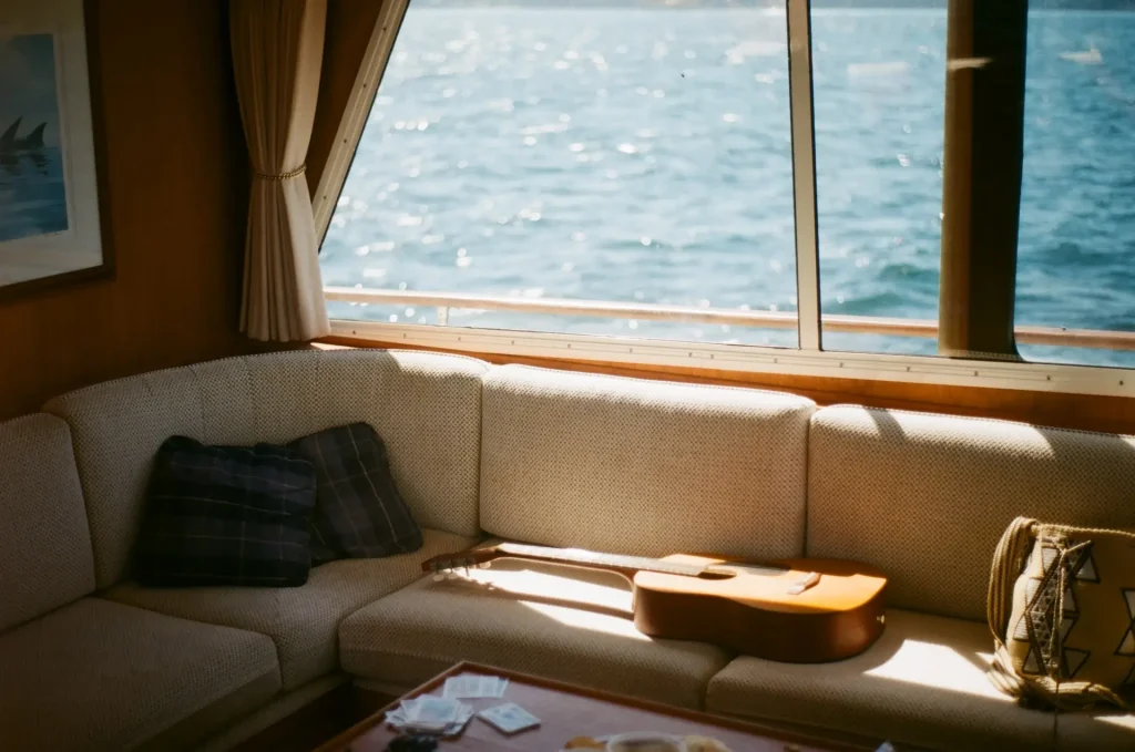 A sun-drenched guitar on a couch under a window overlooking the water