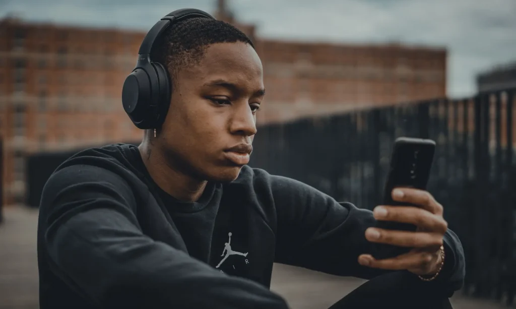 A young man wearing headphones looking at his phone in his hand
