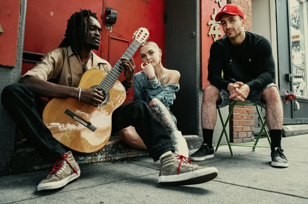 A man sitting on the ground playing a guitar next to a woman and another man