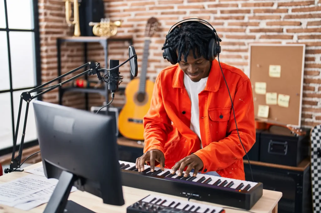 A man wearing headphones playing a piano keyboard in a home recording studio