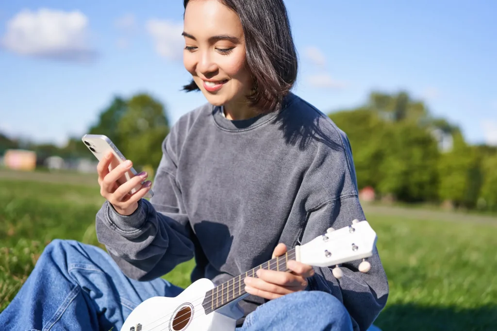 A young woman holding a ukulele and looking at her mobile phone