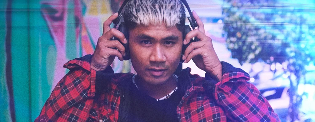A man facing forward, wearing headphones he's holding up to his ears